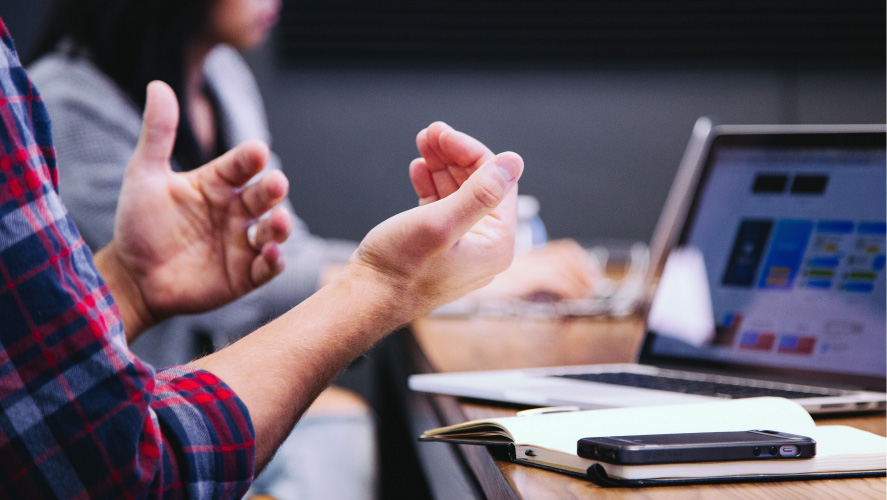 Une personne faisant des gestes à un bureau avec un ordinateur portable, engagée dans un travail ou une communication, mettant en avant la productivité.